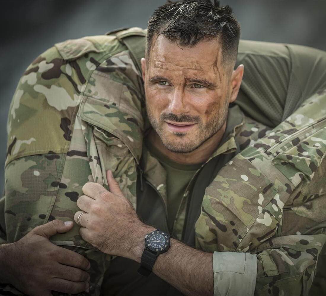 En robust mann i militæruniform bærer en annen person på skuldrene, og viser besluttsomhet og styrke.