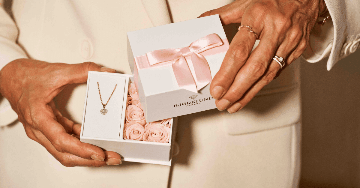 En kvinne med rosa kjole holder en hvit gaveeske med rosa bånd på utsiden og rosa roser på innsiden