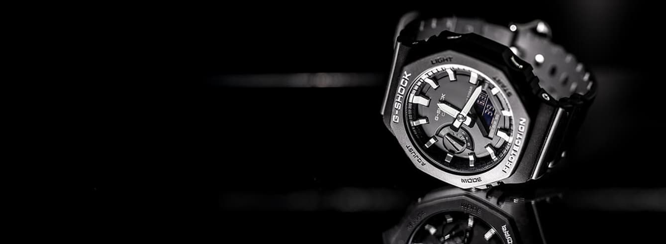 En sølvfarget G-Shock-klokke med digital-analog urskive vises mot en svart reflekterende overflate.