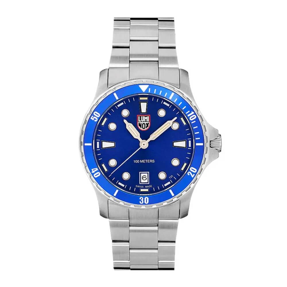 Sølvfarget armbåndsur med blå urskive, selvlysende visere og datovisning. Har Luminox-logo og lenke i rustfritt stål. Vannbestandig ned til 100 meter.