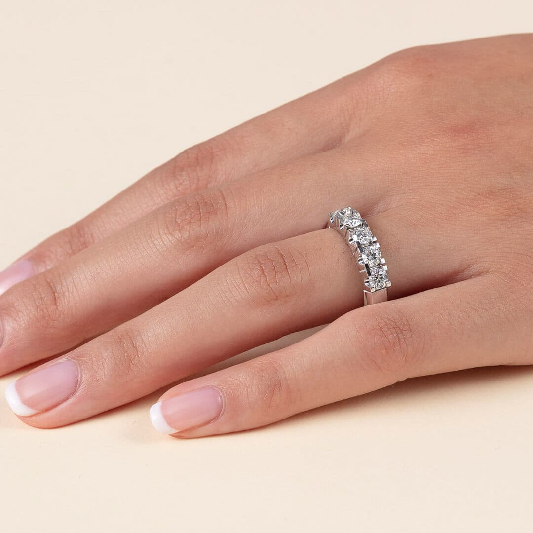 En hånd med fransk manikyr iført en sølvring utsmykket med fem glitrende edelstener på en lys bakgrunn.