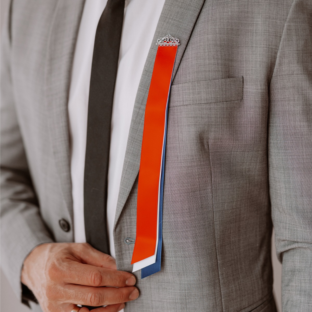 Rød, hvit og blå sløyfe med sølvfarget filigrandekor øverst, avbildet mot hvit bakgrunn.