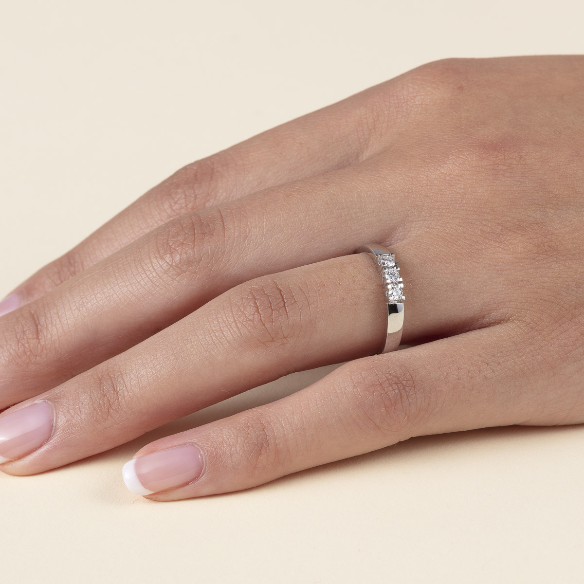 En blank ring i lyst metall med tre runde steiner på rad, festet i fire klør hver, plassert på midten av ringskinnen.