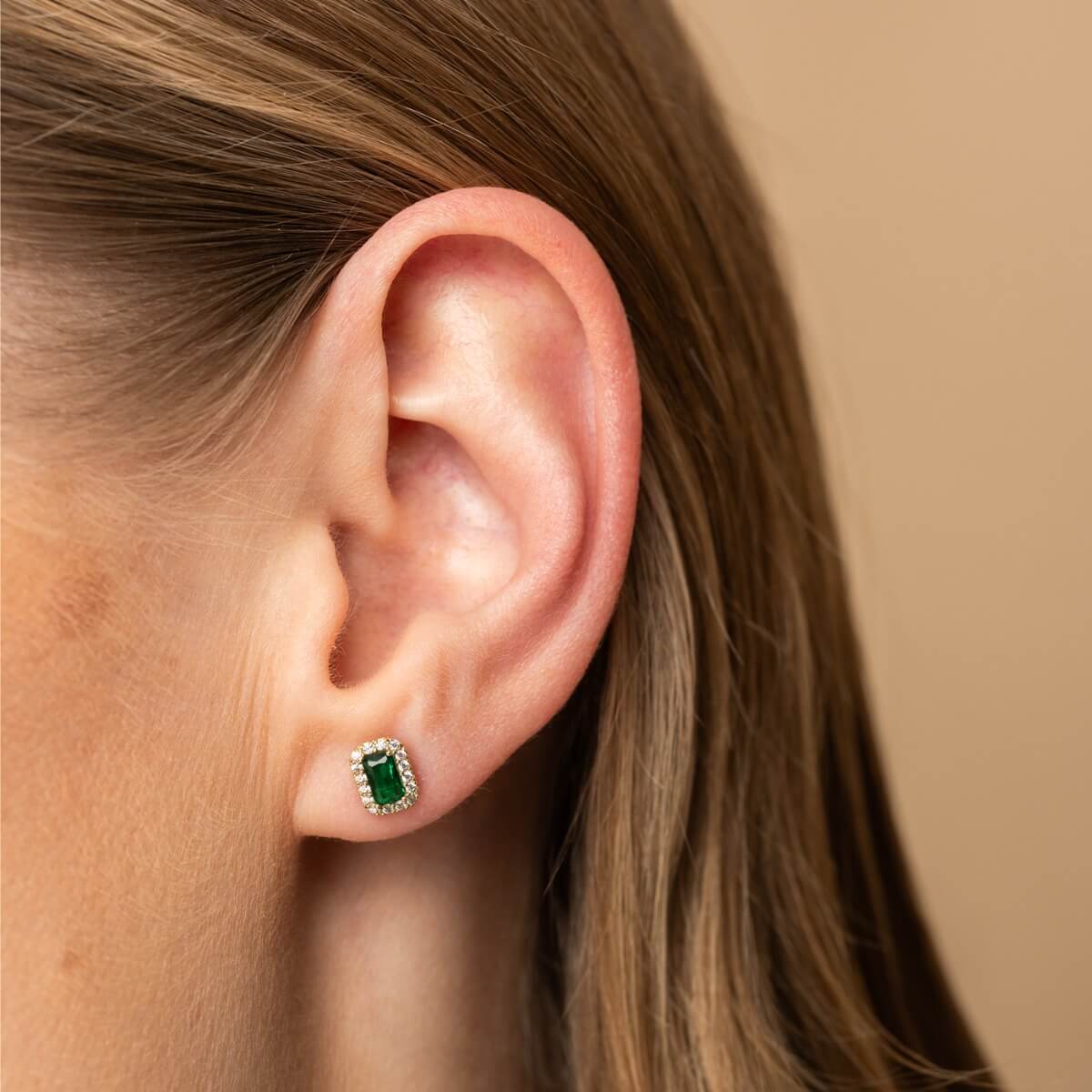 To øredobber i gult gull med rektangulær grønn stein omgitt av små klare steiner i rosettform, vist mot hvit bakgrunn.