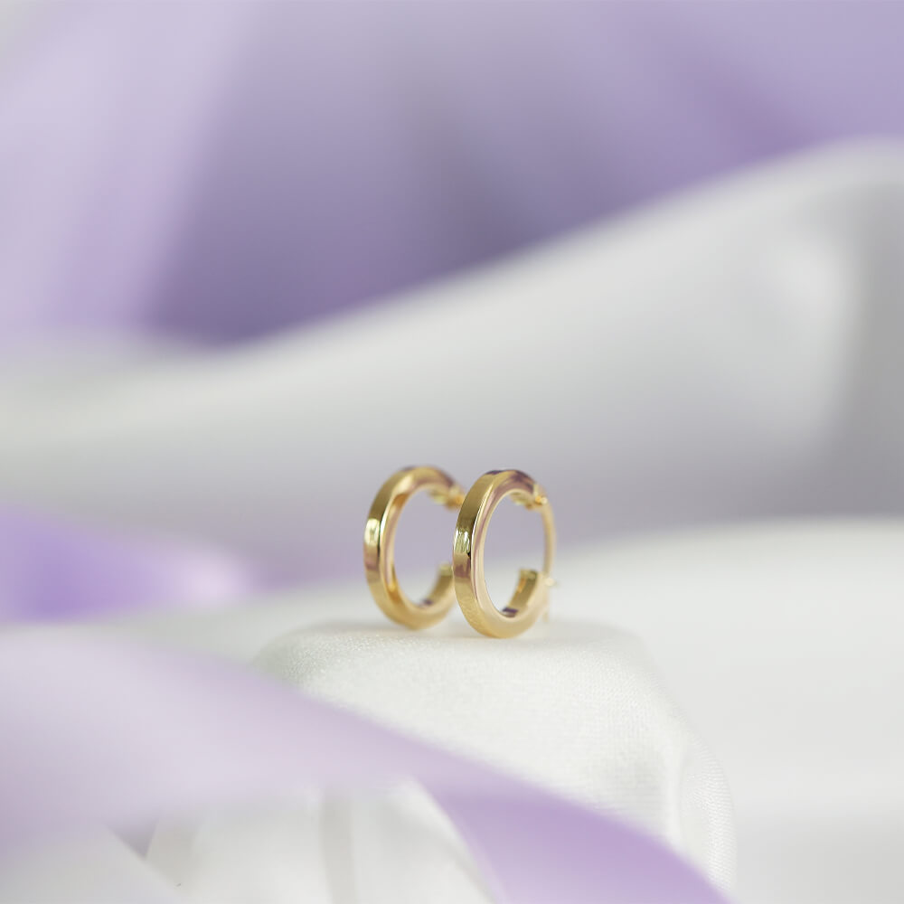 Et par små, sirkelformede øredobber med blank gullfarget overflate og enkel låsemekanisme, vist på hvit bakgrunn.