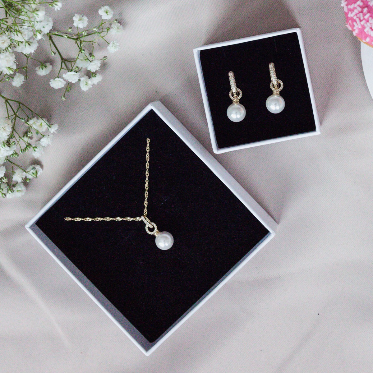 Par med gullfargede hengende øredobber med store hvite perler og små klare steiner på bøylene, avbildet mot hvit bakgrunn.