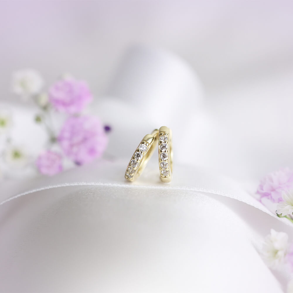 Et par små gullfargede øreringer med blank overflate og små klare stener foran.