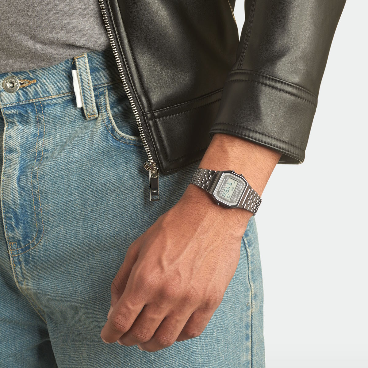 Digital klokke i svart metall med rektangulær skjerm og lenkearmbånd, viser klokkeslett og dato på en lys display.