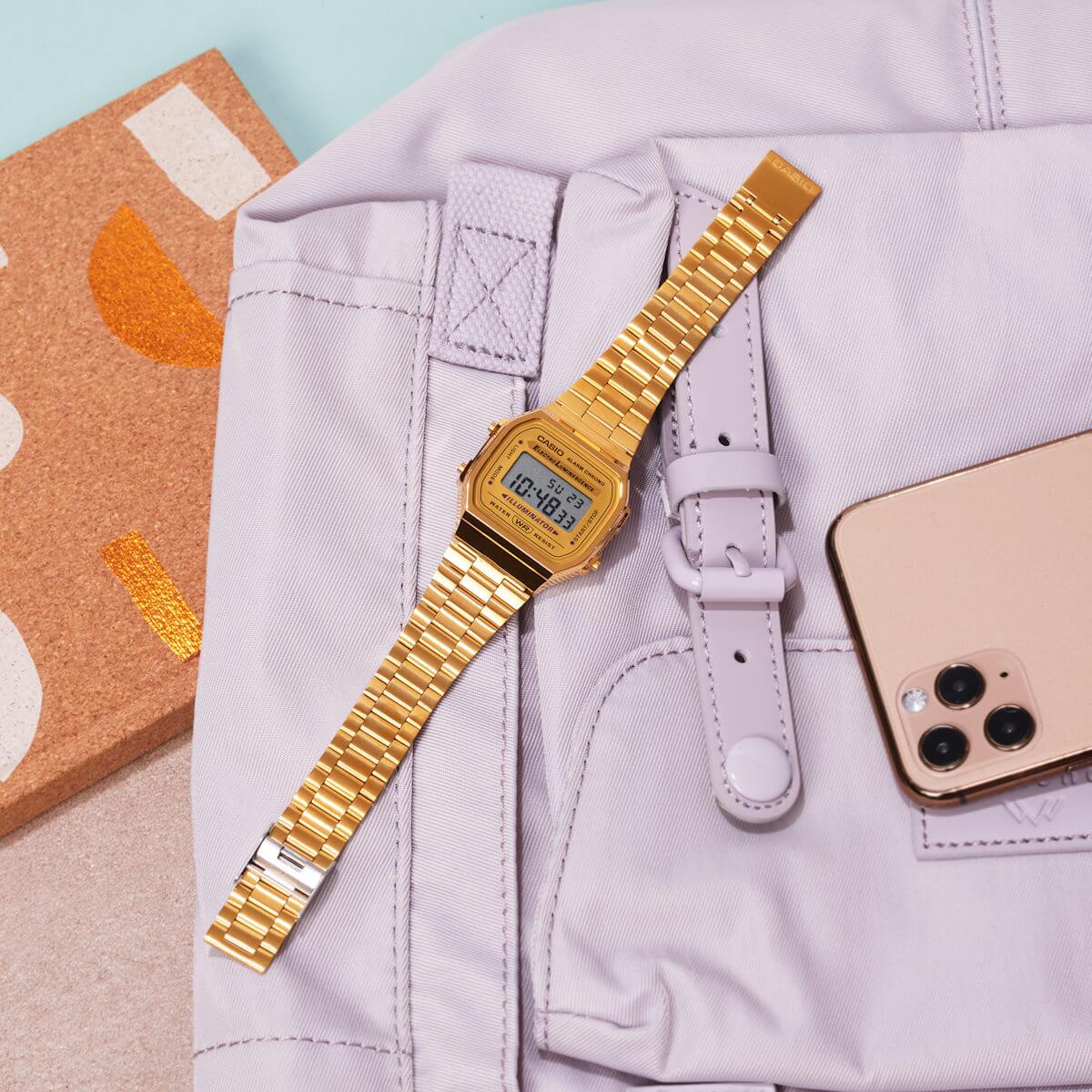 Gullfarget digital armbåndsur med rektangulær skjerm og leddet metallrem, vist forfra mot hvit bakgrunn.