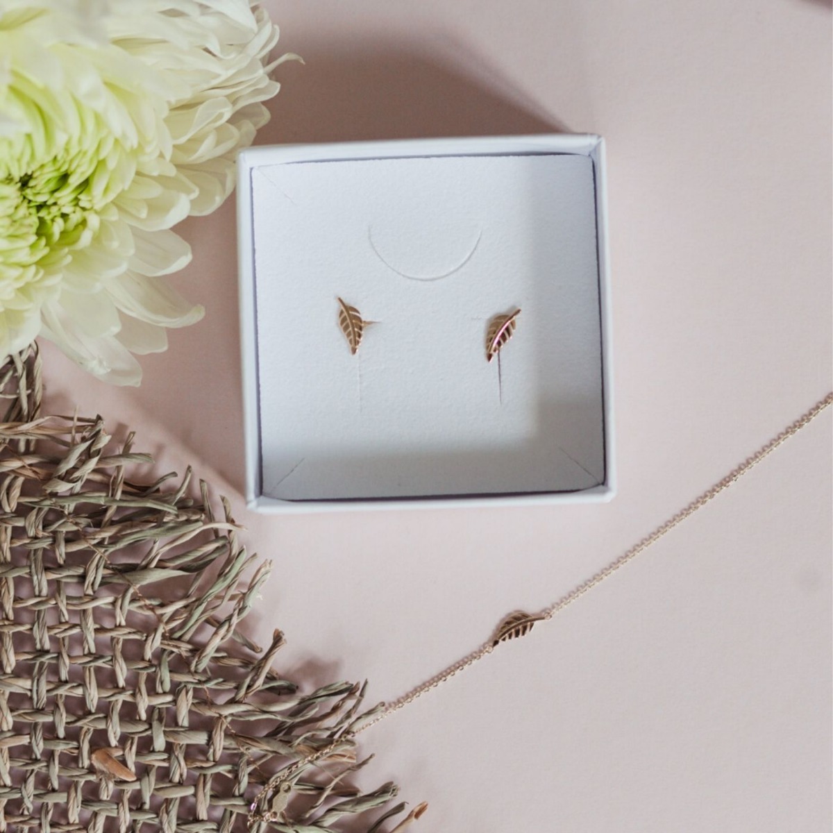 Gullarmbånd med tynn lenke og lite bladformet anheng, vist flatt mot hvit bakgrunn med karabinlås.