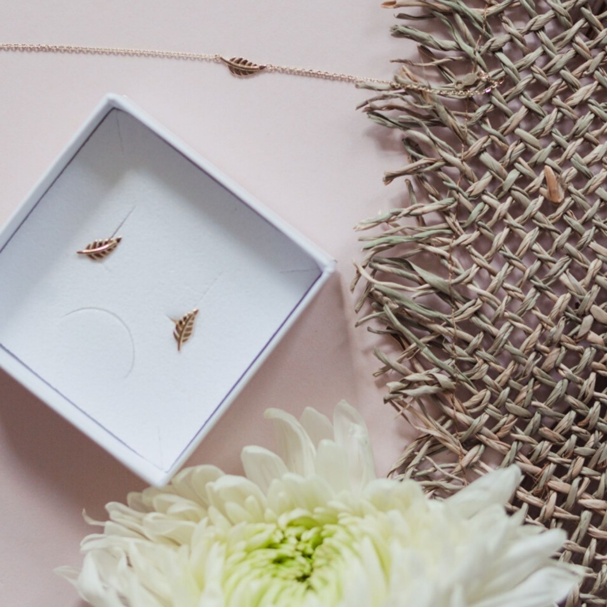 Gullarmbånd med tynn lenke og lite bladformet anheng, vist flatt mot hvit bakgrunn med karabinlås.