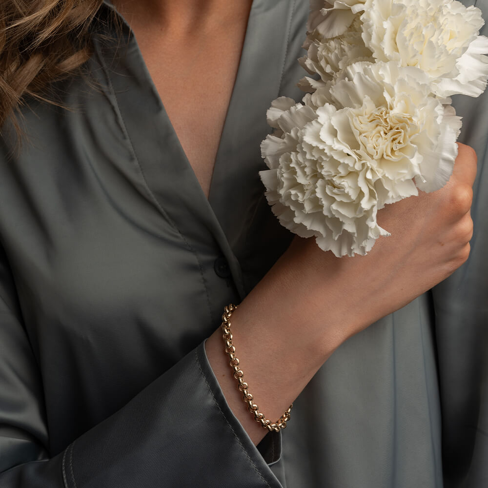 Gullfarget armbånd med små, runde lenker i jevn kjedeform, vist liggende i sirkel mot hvit bakgrunn.