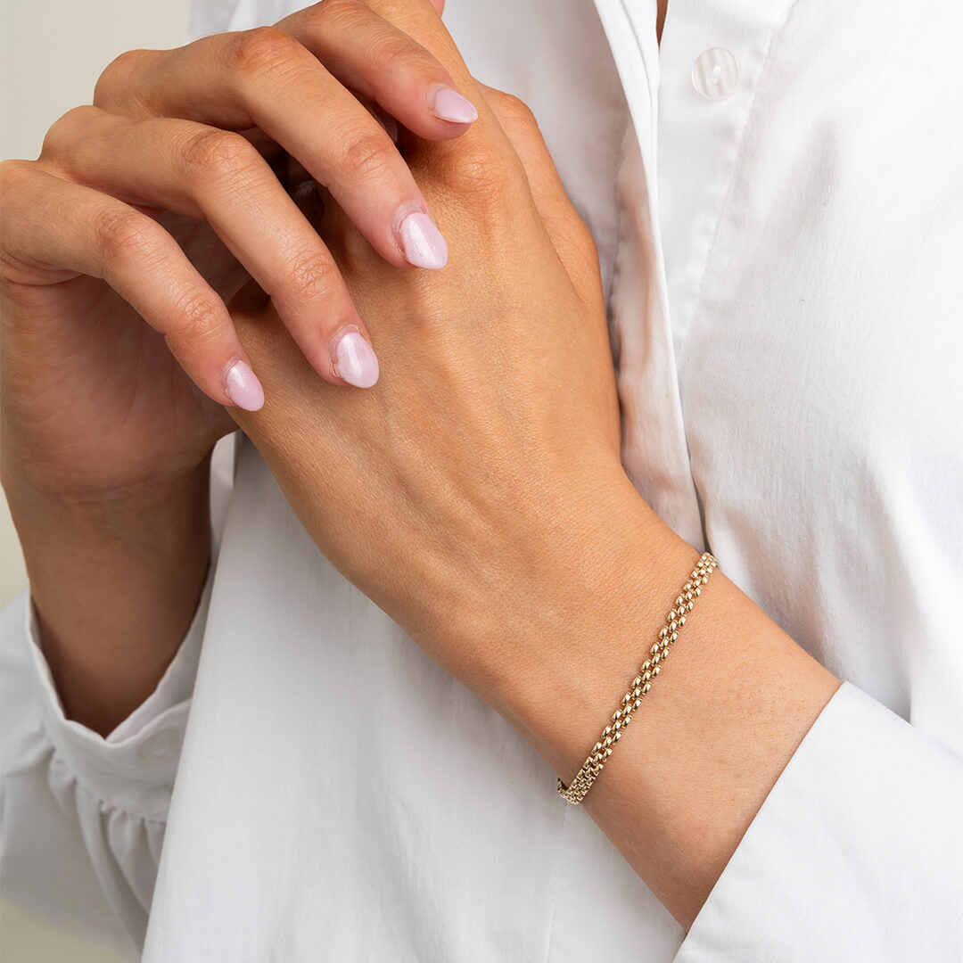 Gullfarget armbånd med tett flettet kjede og karabinlås, formet i sirkel mot hvit bakgrunn.