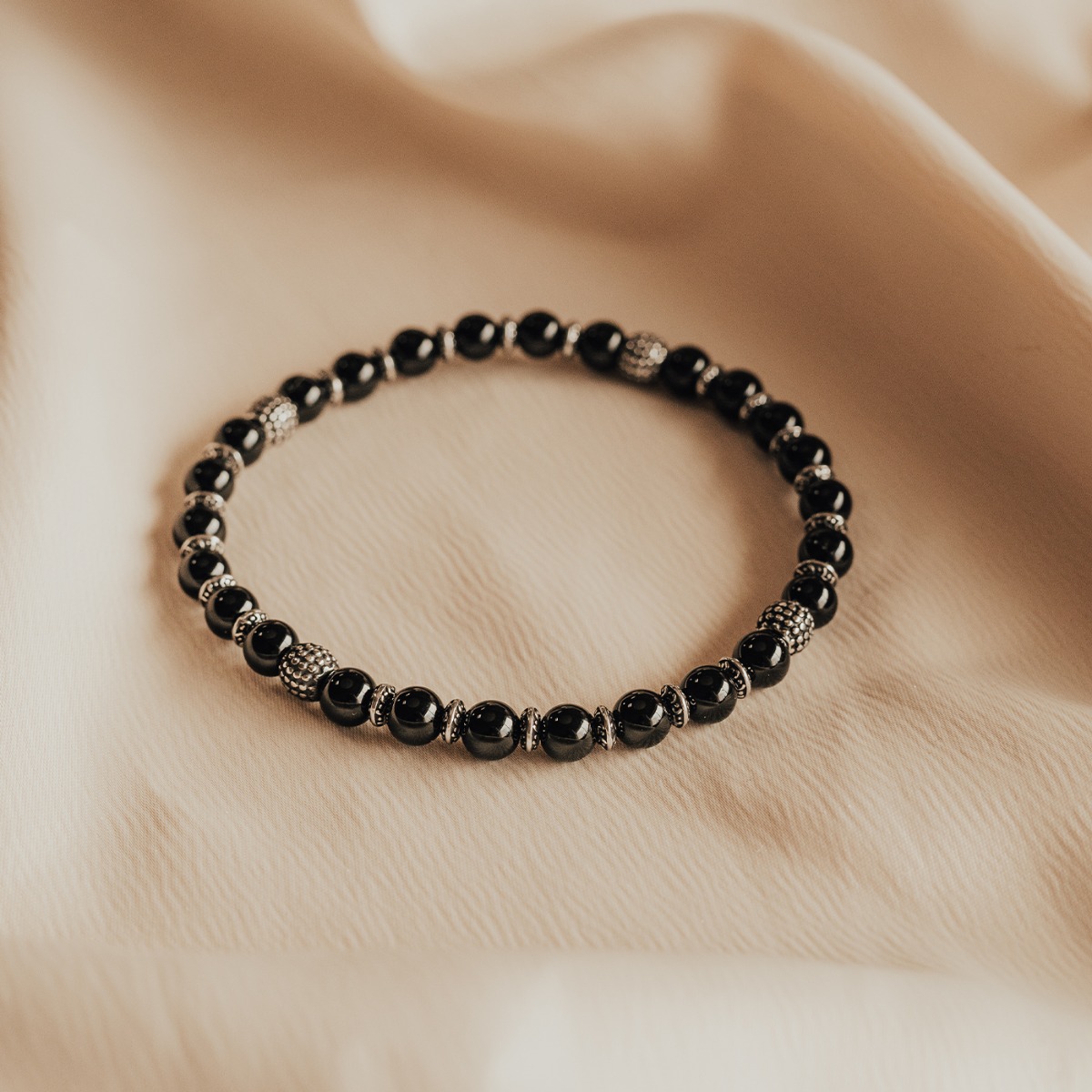 Elastisk armbånd med svarte kuler og detaljerte sølvfargede perler i metall, vist mot hvit bakgrunn.