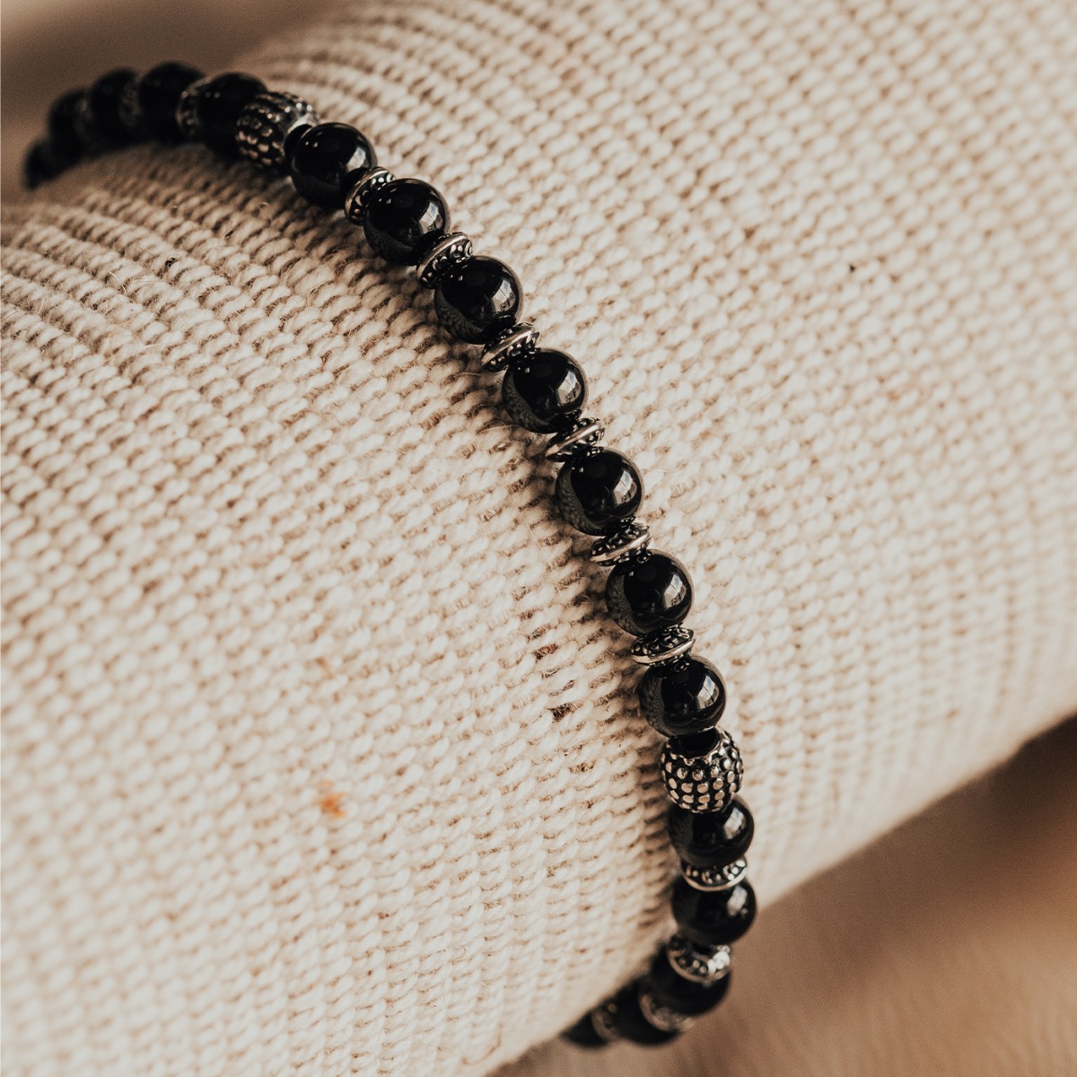 Elastisk armbånd med svarte kuler og detaljerte sølvfargede perler i metall, vist mot hvit bakgrunn.