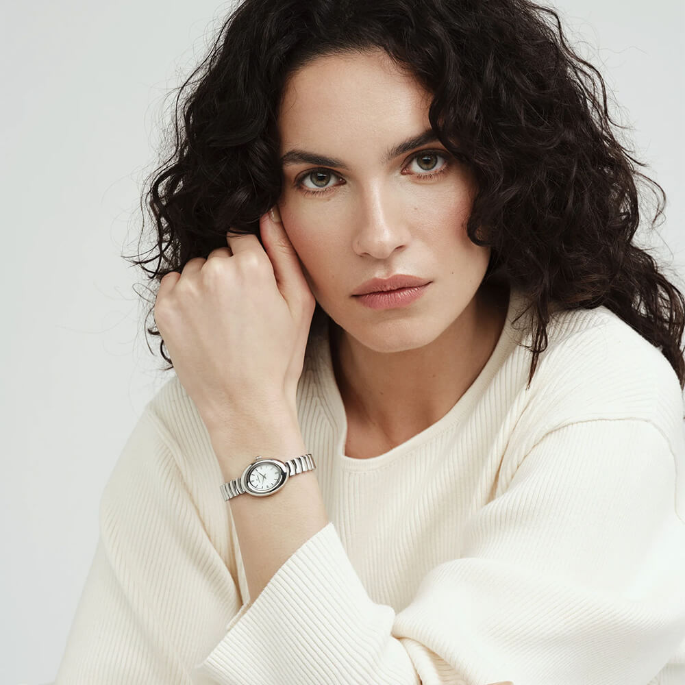 Sølvfarget klokke med oval urskive og lenke vises mot hvit bakgrunn, med skygge under som gir en svevende effekt.