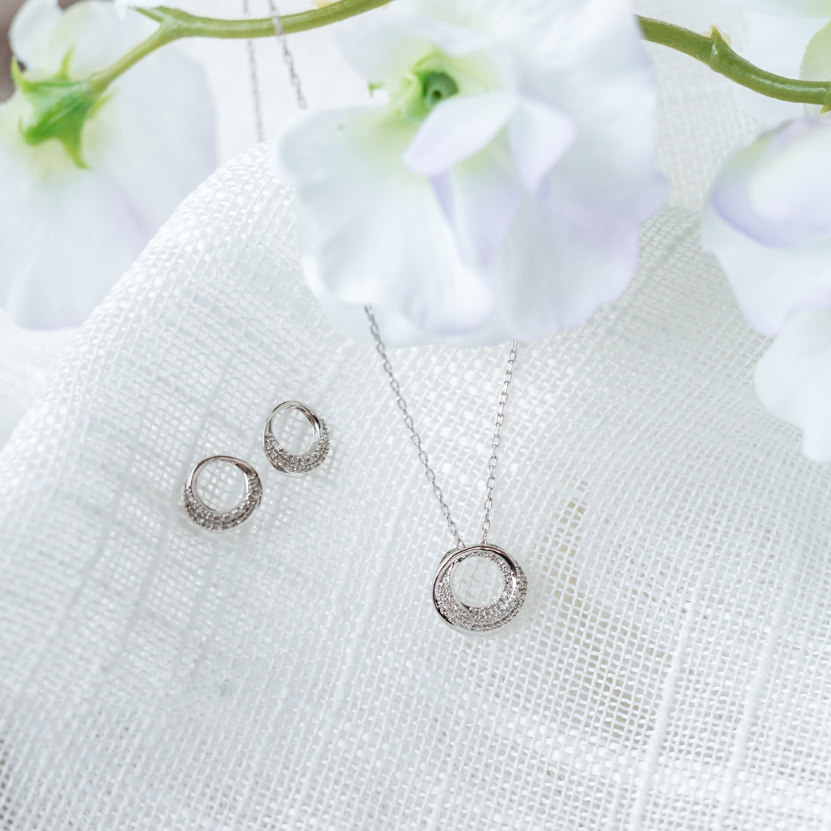 Et par runde øredobber i hvitt gull med to rader små diamanter i nedre del av sirkelen, vist på hvit bakgrunn i vinkel.