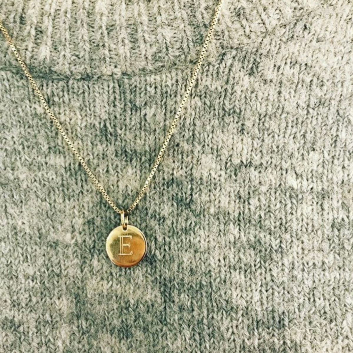 Gullfarget kjede med rundt, flatt anheng uten gravering, festet i en liten ring og avbildet mot hvit bakgrunn.