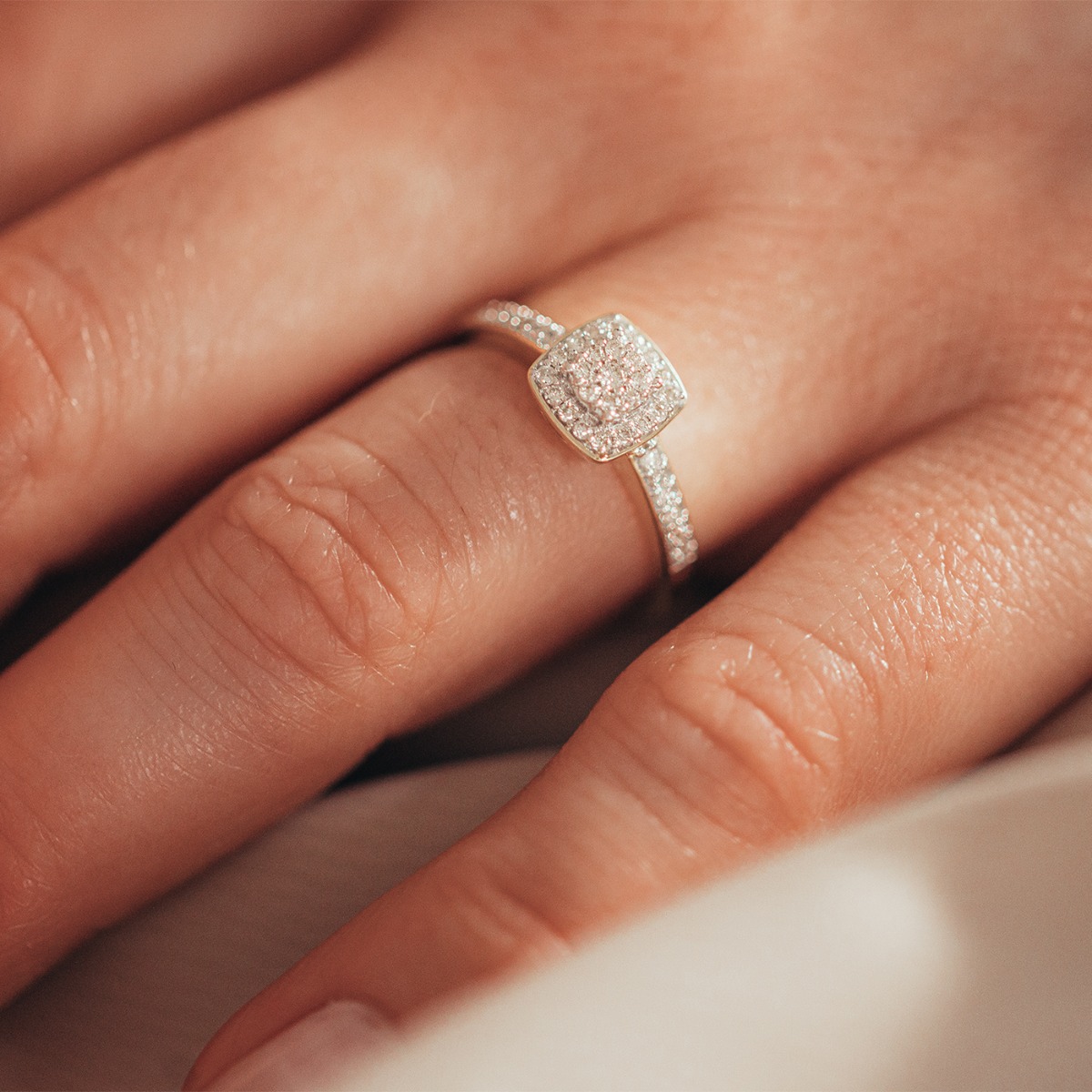 Sølvring med firkantet fatning dekorert med små diamanter og diamantbesatte skuldre, avbildet mot hvit bakgrunn.