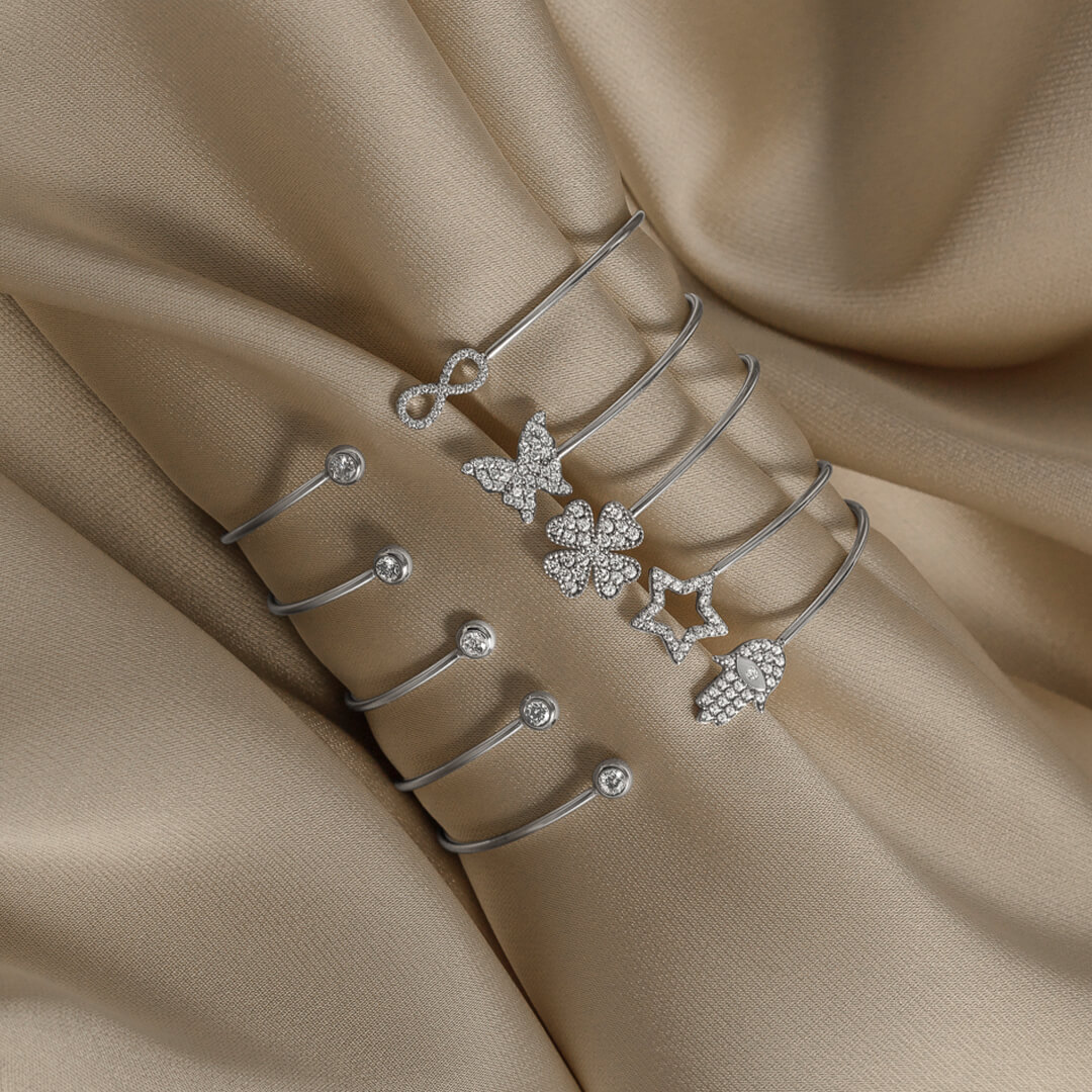 Tynn, åpen armring i sølvfarge med sirkel med klar stein på den ene siden og liggende åttetall pyntet med små steiner på den andre.