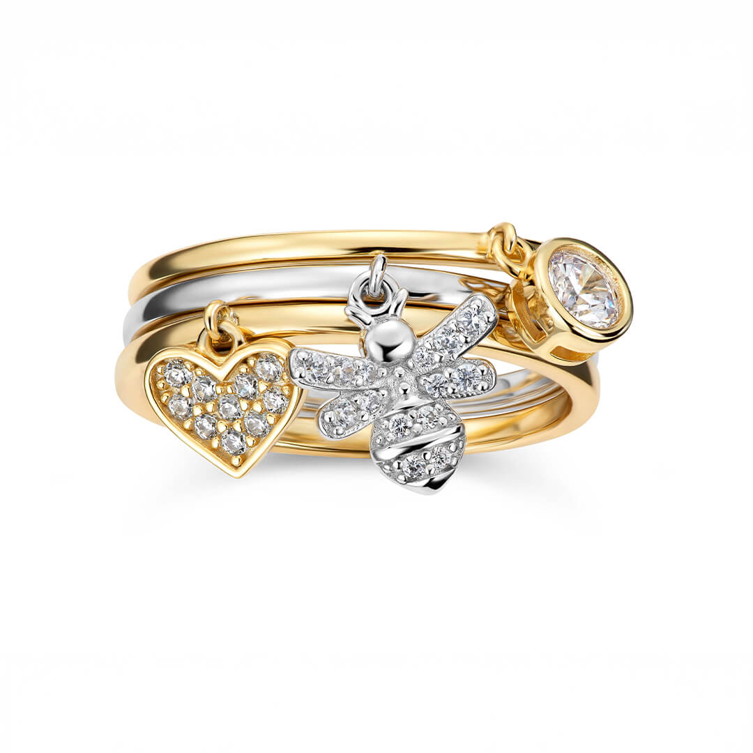 Gullfarget ring med glatt overflate og en liten hjerte charm med klar stein som henger ned fra midten av ringen.