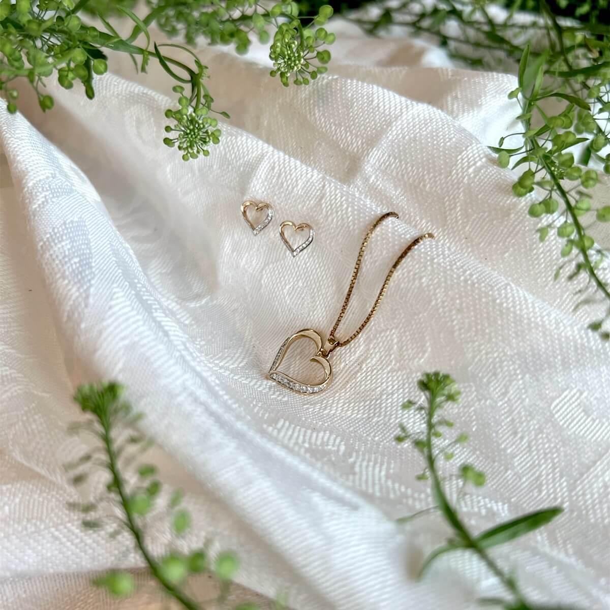 Diamantsmykke i gult gull med åpen hjerteformet anheng og små steiner i nedre del, avbildet mot hvit bakgrunn.