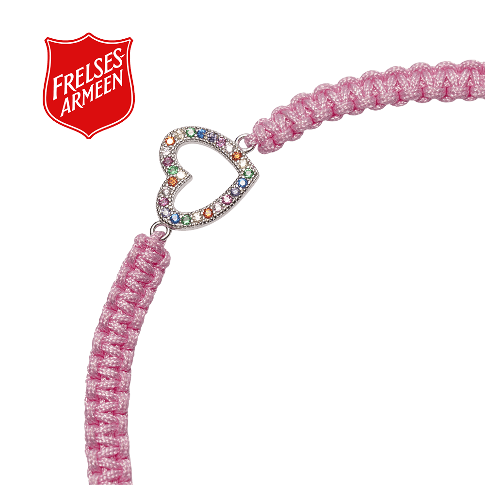 Et Frelsesarmeen vennskapsarmbånd i rosa med fargerikt hjertesmykke på hvit bakgrunn og rød Frelsesarme-logo øverst til venstre.