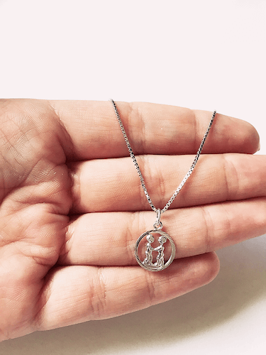 Sølvfarget kjede med rundt anheng som viser stjernetegnet Tvillingene, liggende mot hvit bakgrunn.