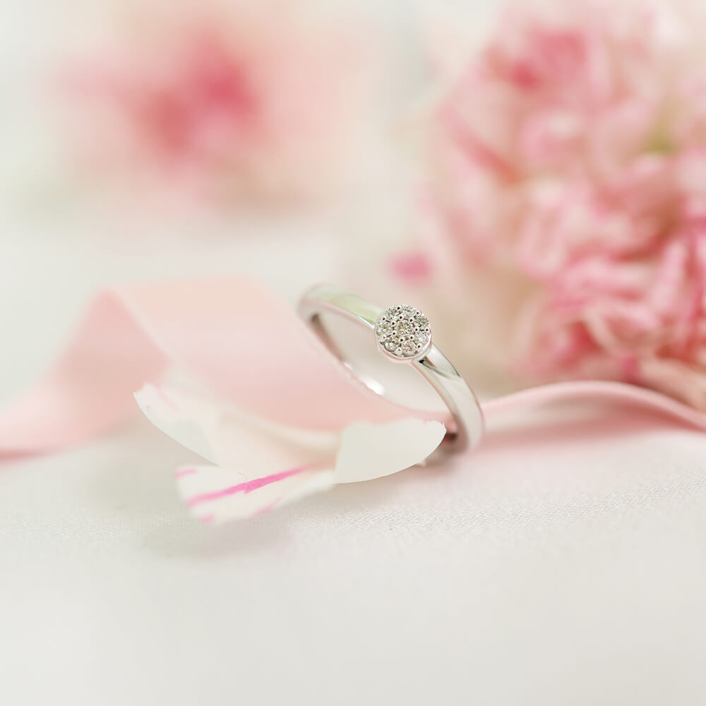 Ring med glatt ringskinne og liten rund klynge av diamanter i senter, avbildet mot hvit bakgrunn.