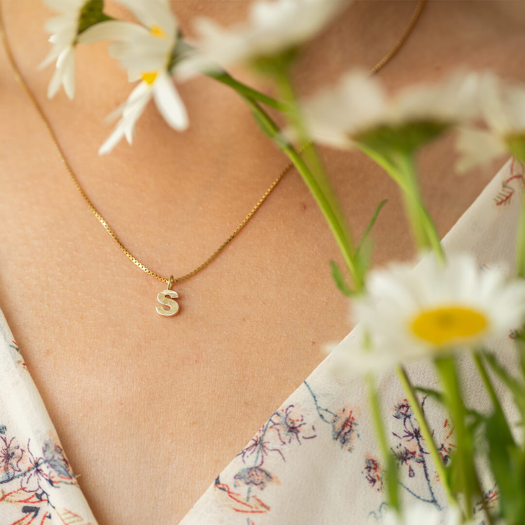 Halssmykket med kjede og anheng av bokstaven S i gullfarge.