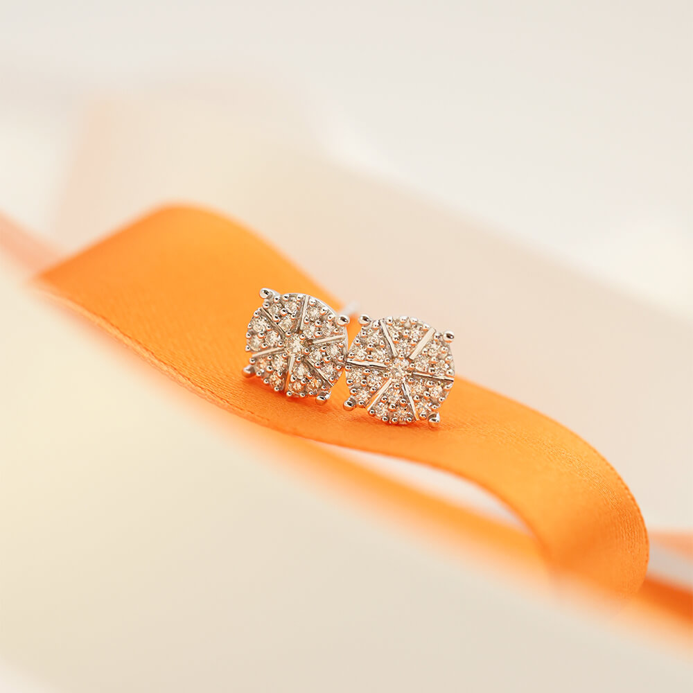 Et par øredobber i hvitt metall med runde diamantklynger, stjerneformet innfatning og stiftfeste, avbildet på hvit bakgrunn.