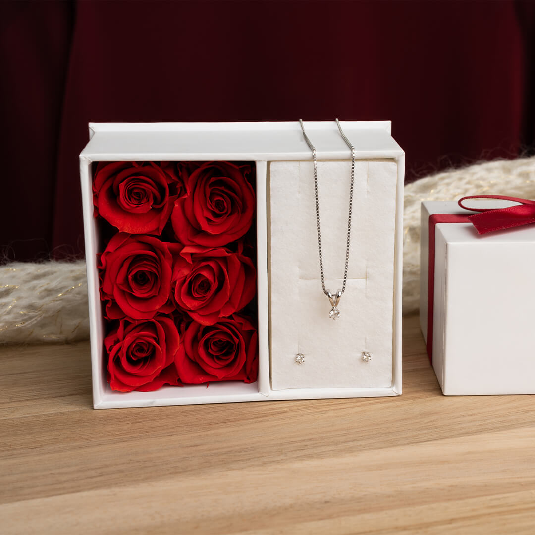 Par øredobber i metall med små runde diamanter i seks klør, vist liggende på hvit bakgrunn med speiling.