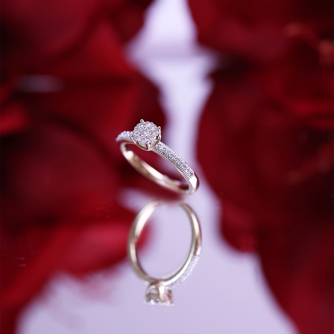 Gullring med rund klynge av diamanter i midten og små diamanter på begge sider av ringskinnen.