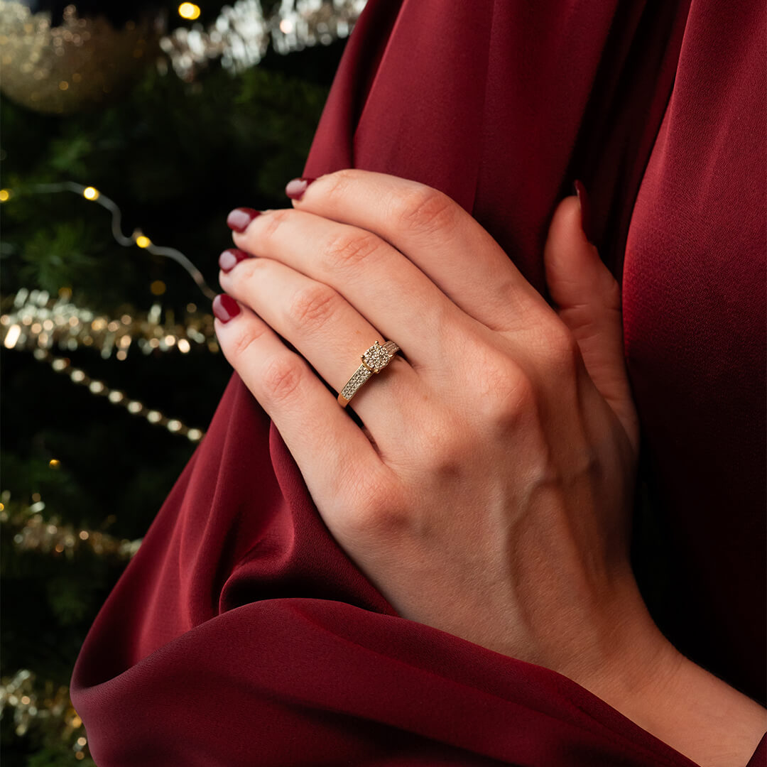 Gullring med rund midtsten omgitt av små klare stener, og flere små stener satt tett i rekker langs ringskinnen.