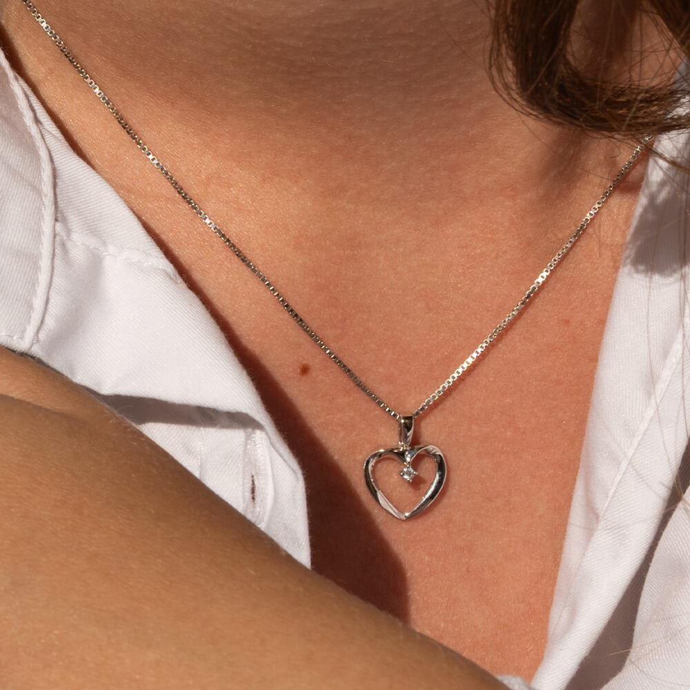 Halskjede i hvitt gull med åpent hjerteanheng og liten diamant i midten, avbildet mot hvit bakgrunn. 