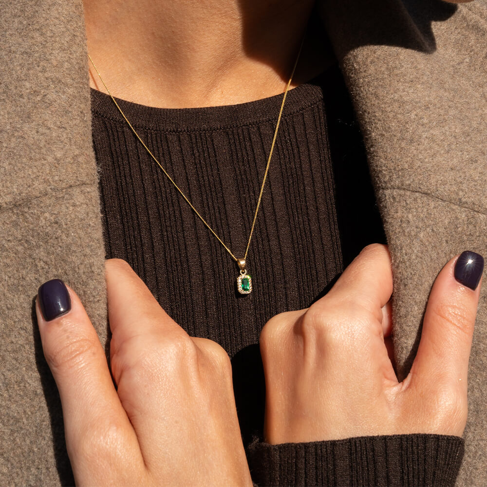 Halskjede i gult gull med rektangulært anheng med grønn midtstein omgitt av små klare stener i rosettfasong.