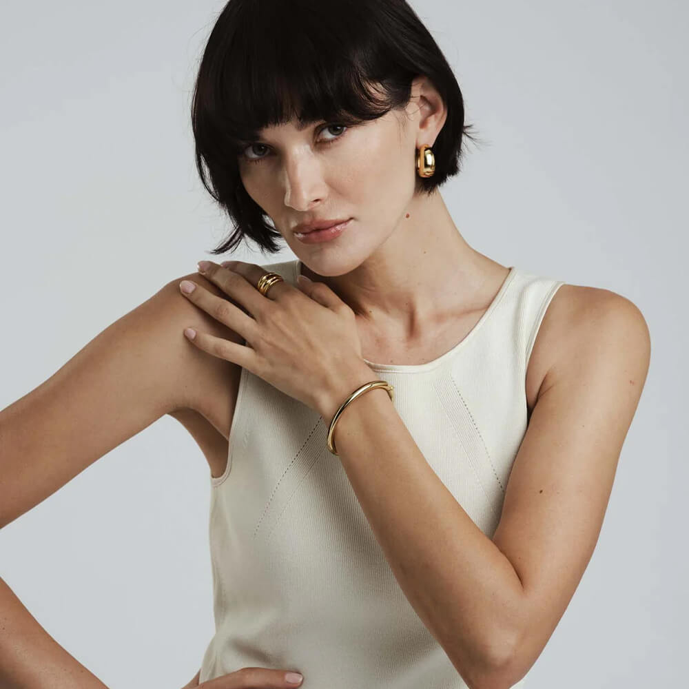 Rundt, skinnende gullarmbånd med jevn overflate, avbildet liggende mot hvit bakgrunn.