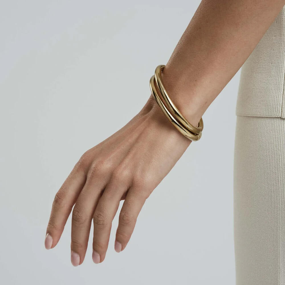 Rundt armbånd i skinnende gullfarge med jevn overflate, avbildet liggende mot hvit bakgrunn.