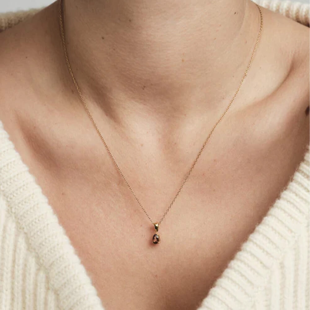 Gullkjede med dråpeformet brun sten i klofatning, hengende mot hvit bakgrunn for produktvisning. 