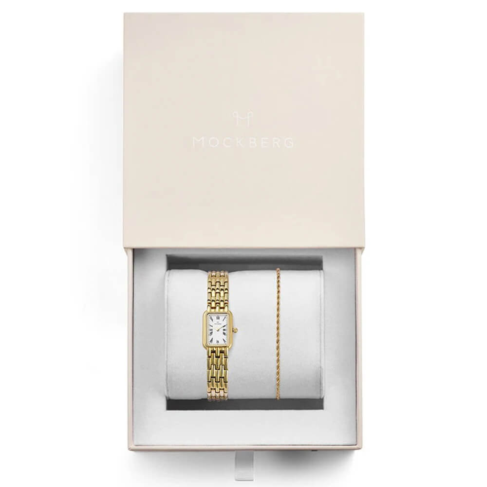 Gullfarget armbåndsur med hvit urskive og tynn lenke plassert i en lys gaveeske med hvit pute og Mockberg-logo.