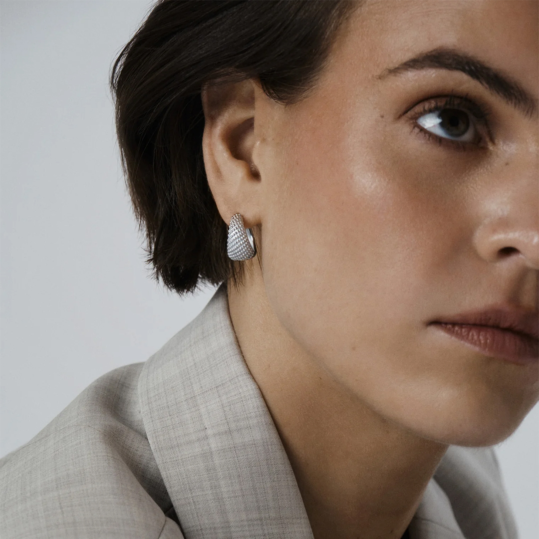 Et par brede øreringer i sølv med prikker og ruglete overflate.