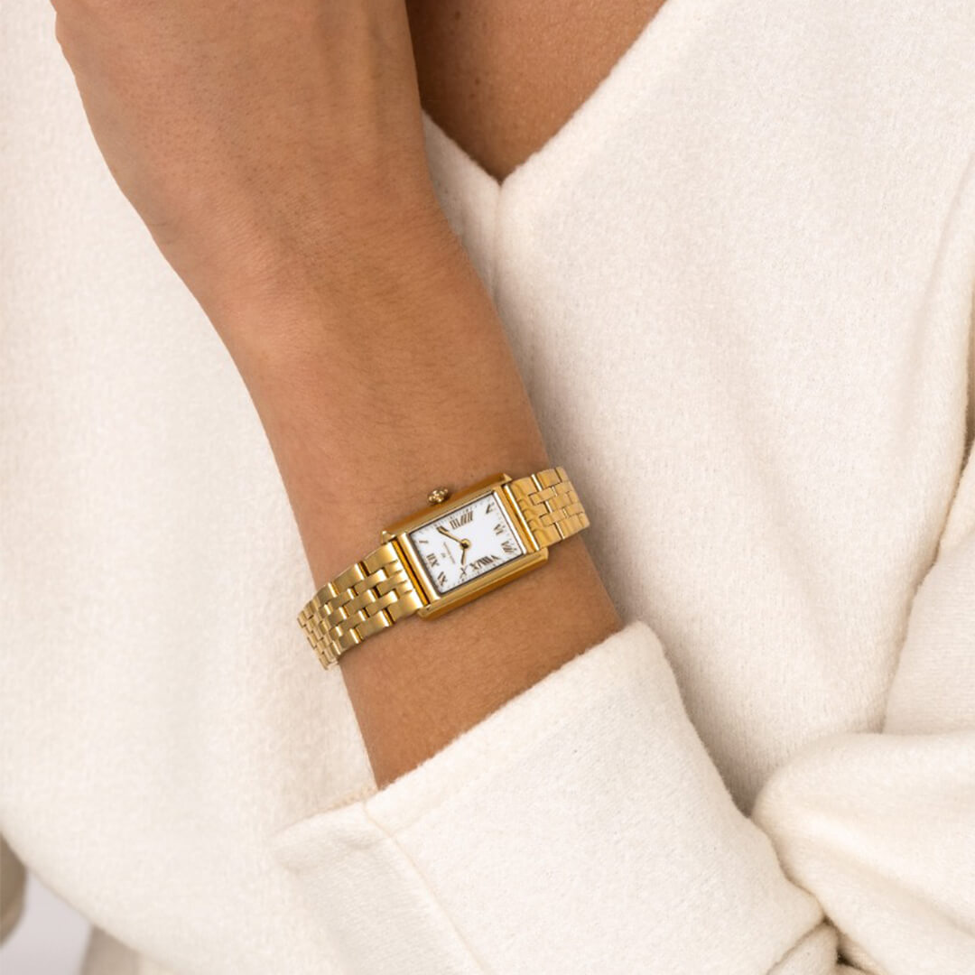 Rektangulær gullfarget armbåndsur med hvit urskive og romertall, vist mot hvit bakgrunn