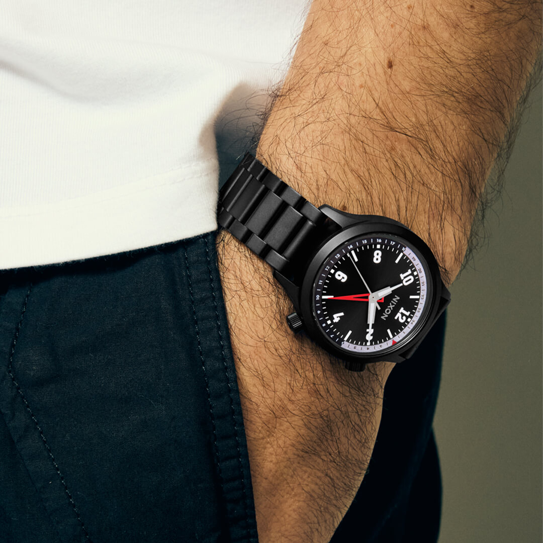 Nixon klokke i sort metall med hvite tall, rød GMT-viser, grå 24-timers ring, to trykknapper og sort lenke