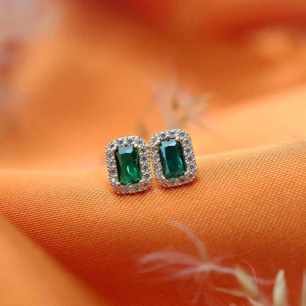 To øredobber i gult gull med rektangulær grønn stein omgitt av små klare steiner i rosettform, vist mot hvit bakgrunn.