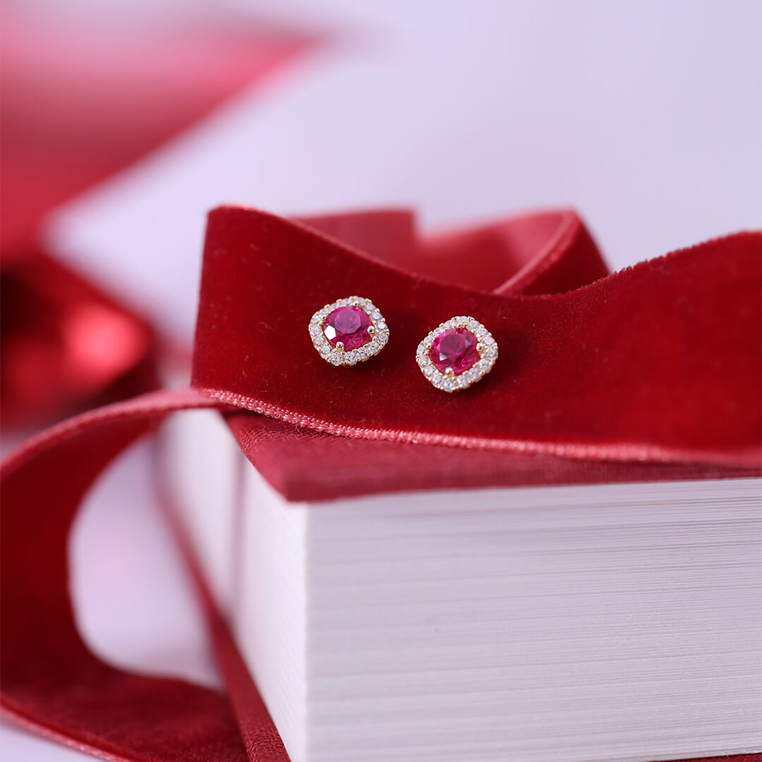 Et par øredobber i gult metall med runde rosa steiner i midten, omgitt av små klare stener i rosettform mot hvit bakgrunn.