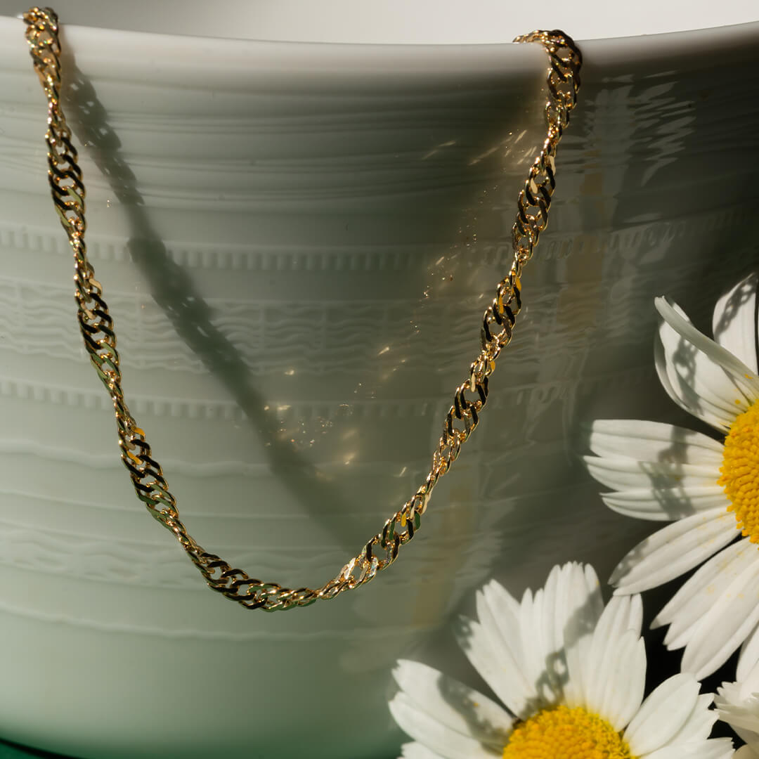 Gullfarget armbånd med flettet mønster og krok-lås vist mot hvit bakgrunn.