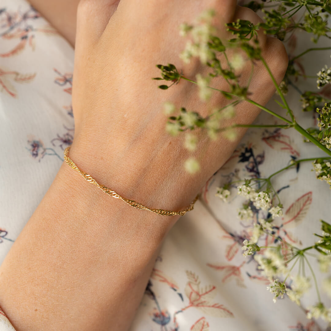 Gullfarget armbånd med flettet mønster og krok-lås vist mot hvit bakgrunn.