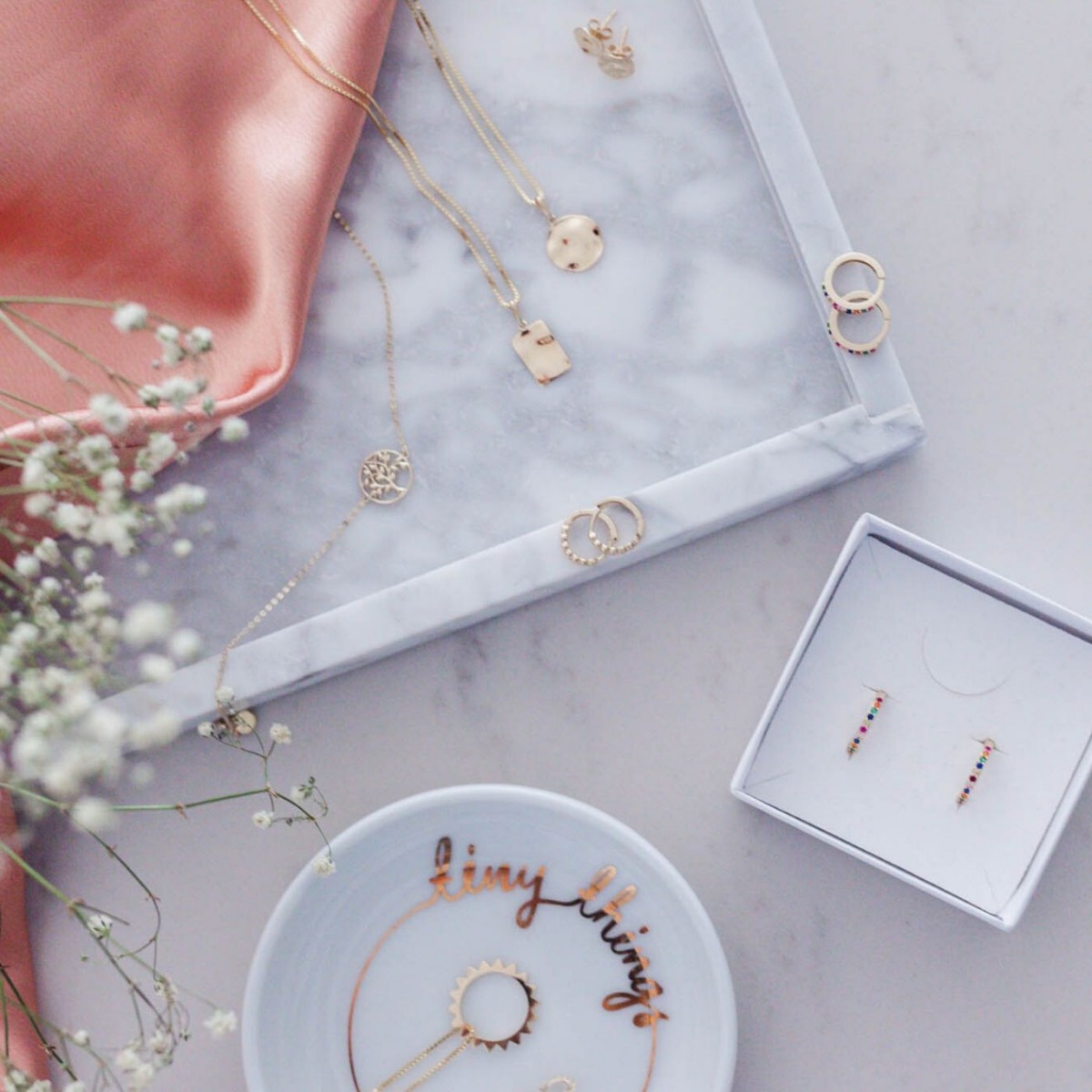 Gullfarget halskjede med tynt kjede og rundt anheng formet som en stilisert sol med taggete ytterkant, fotografert mot hvit bakgrunn.