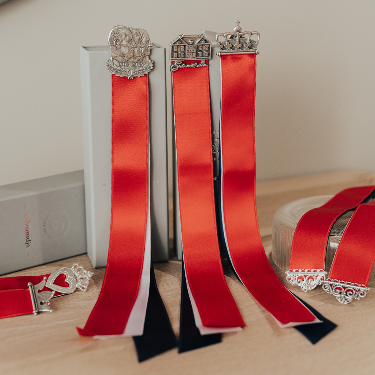 Sølvsløyfe med kroneformet spenne og rødt, hvitt og blått bånd mot hvit bakgrunn