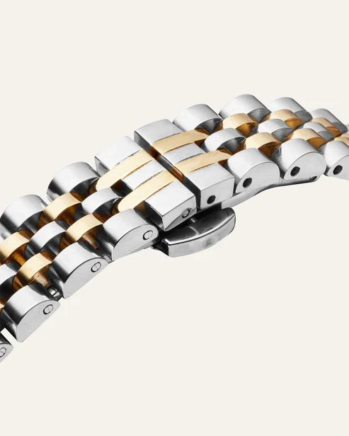 Mockberg-klokke i sølv og gull med beige urskive og liten sekundviser nederst på skiven.